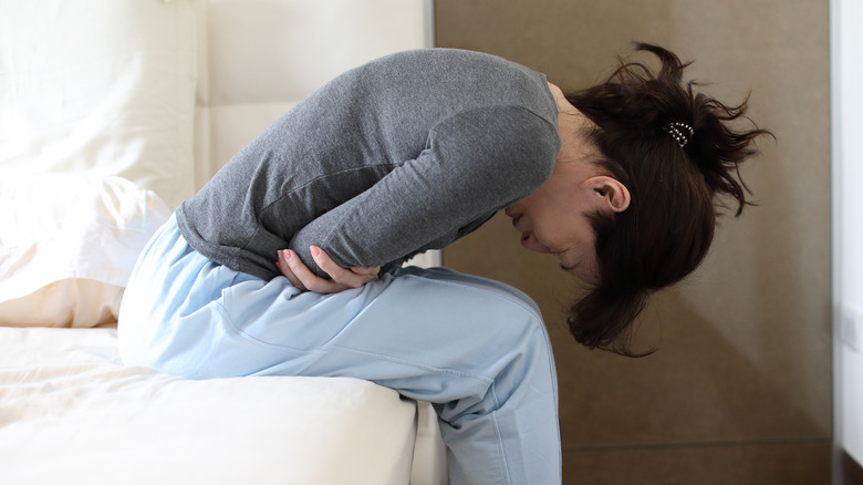 woman leaning over bed in pain