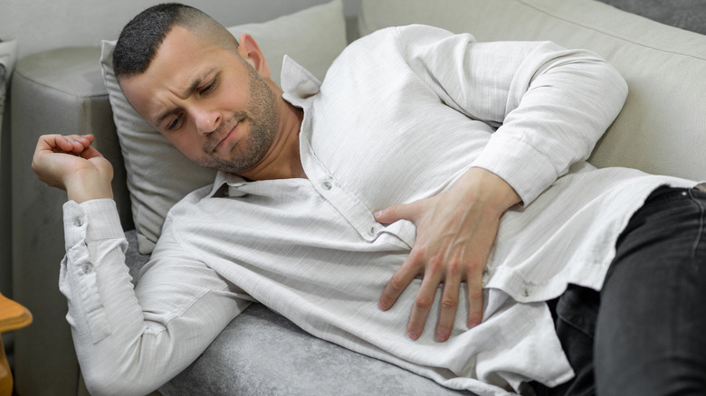 Man on couch rubbing painful stomach 