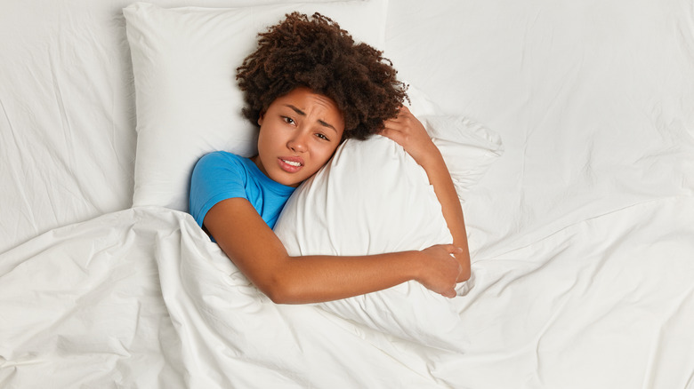 Woman in bed holding pillow, not able to sleep