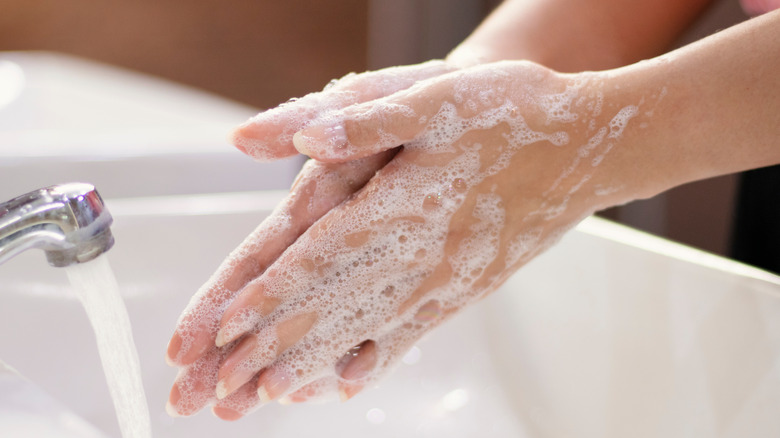 Close up of soapy hands by running faucet