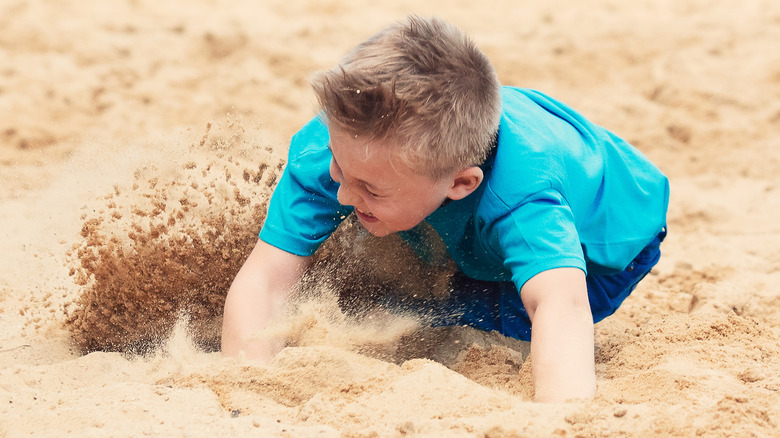Child falling into sand while playing beach volleyball