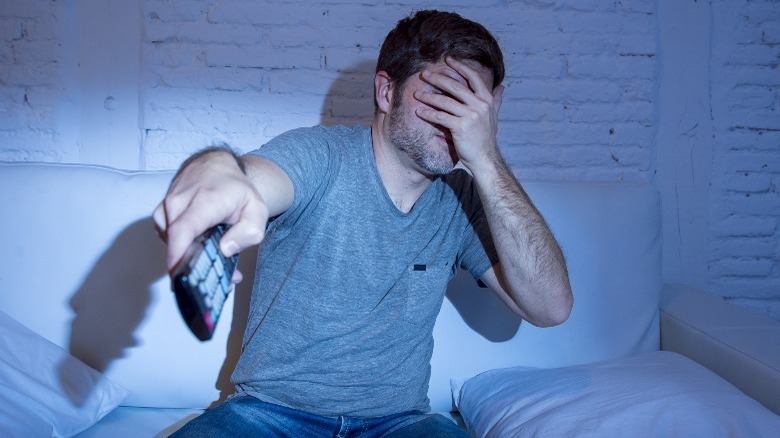 man covering face and switching TV channel