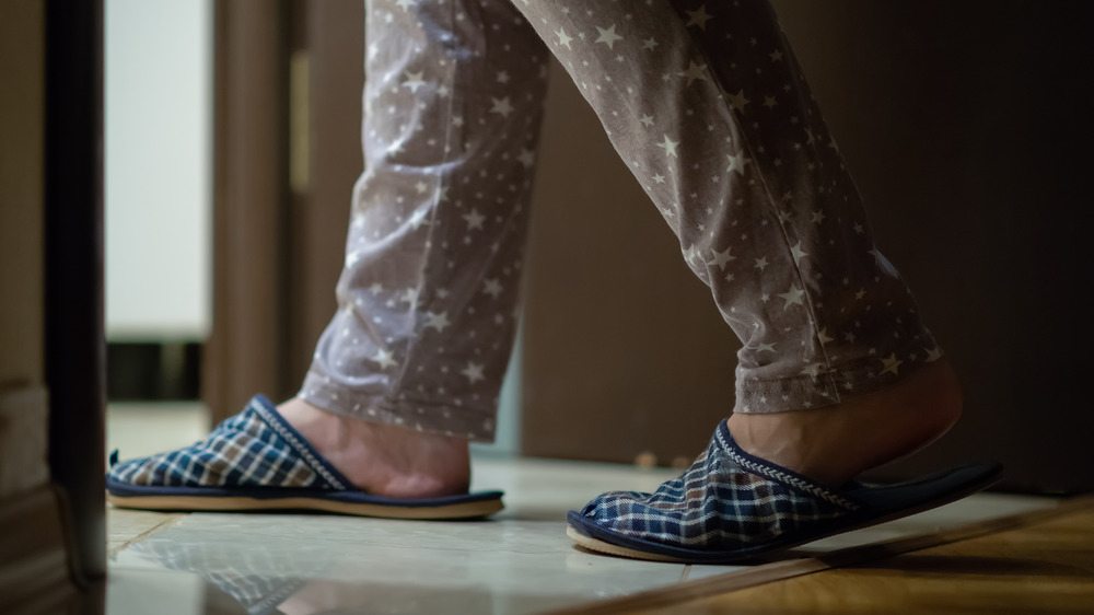 Close up of women's legs and feet in pajamas and slippers going into the bathroom at night