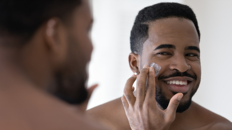 Man looking in mirror smiling applying lotion to cheek