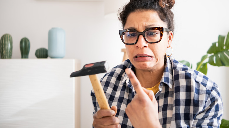 Woman holding hammer and looking at her finger