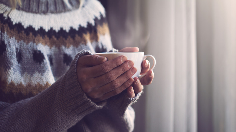 Cold hands holding hot cup of coffee