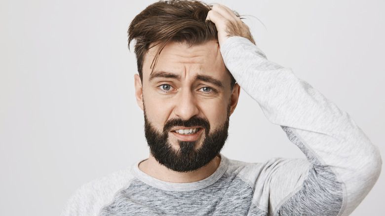 Bearded man in gray and white long sleeved shirt and hand on head