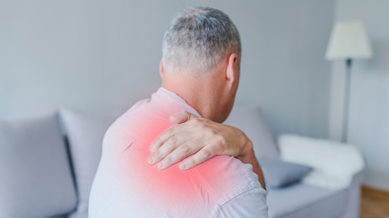 man sitting on the bed and holding painful upper back with another hand