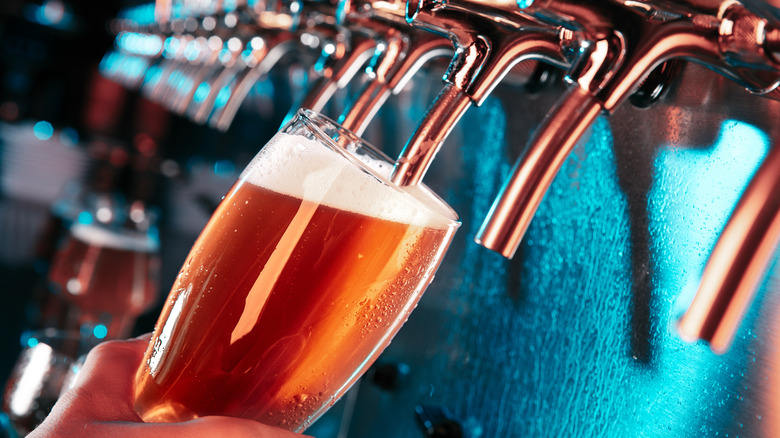 Close up of a hand holding a glass of beer under a tap