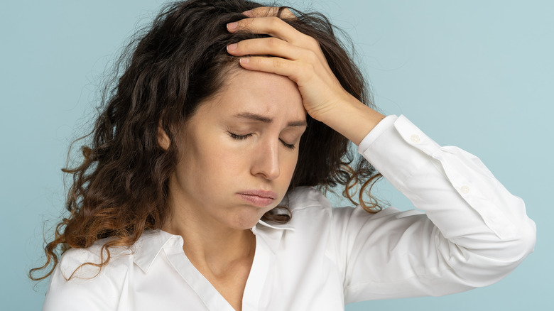 Woman with long hair holding her head in distress against a light blue background