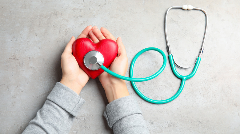 A pair of hands holding a red wooden heart next to a stethoscope