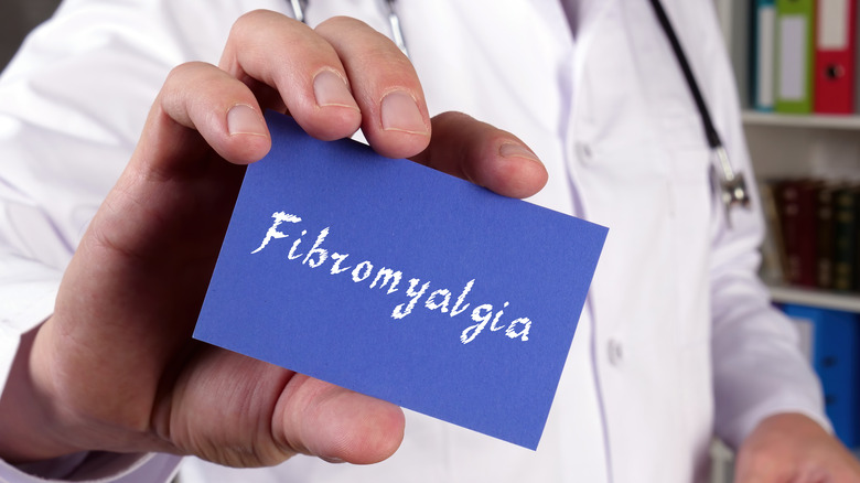 Close up of a doctor's hand holding out a royal blue card with the word "fibromyalgia" written in white lettering 