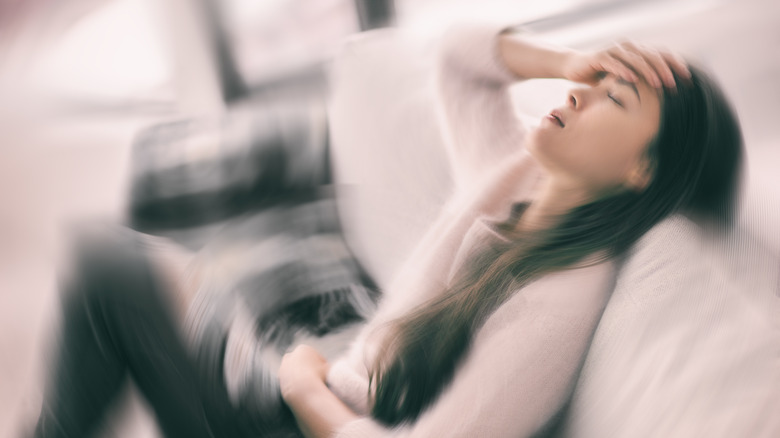 Woman in distress sitting on a couch while holding her head and stomach