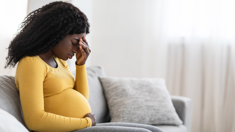 A pregnant woman holding her head while sitting on a couch