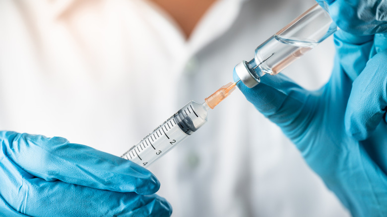 Gloved hands holding syringe and vaccine vial