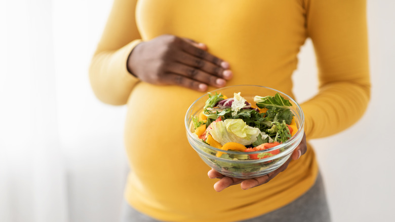 pregnant woman holding her stomach and a bowl of vegetables