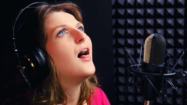 Woman wearing headphones singing into a microphone in a sound booth while sticking out her tongue