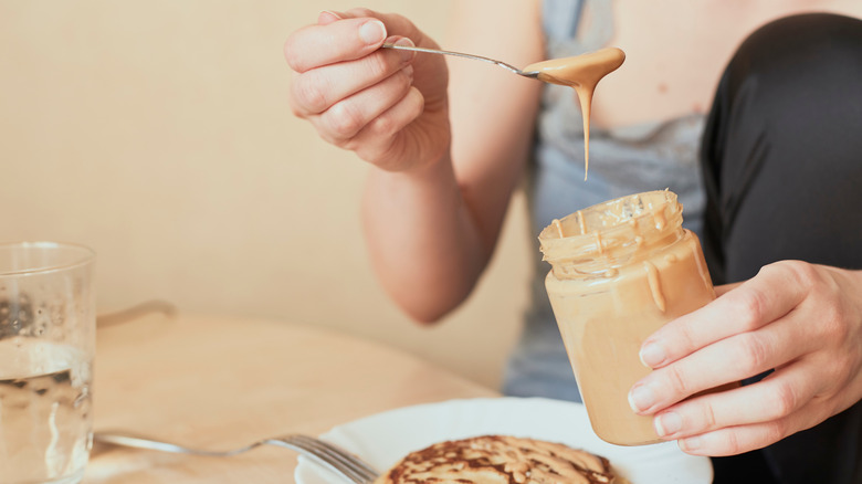 woman topping pancake with peanut butter