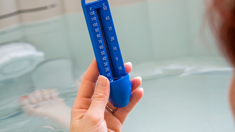 Woman holding thermometer in hot tub bath checking temperature