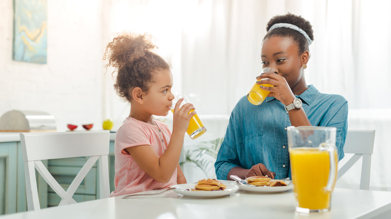 A woman drinks orange juice with her daughter