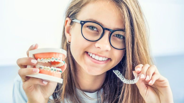 A girl holds an Invisalign tray and a dental model with braces