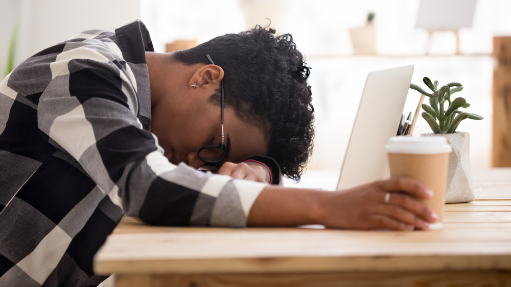 Young male napping at his desk while holding coffee 