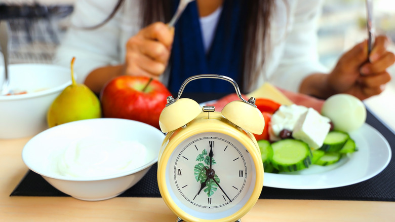 woman eating healthy meal behind a small clock