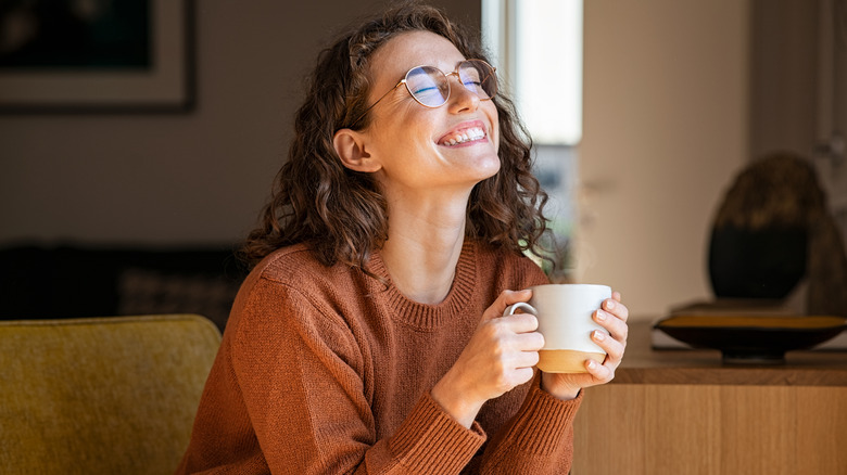 a grinning young woman enjoys a cup of coffee
