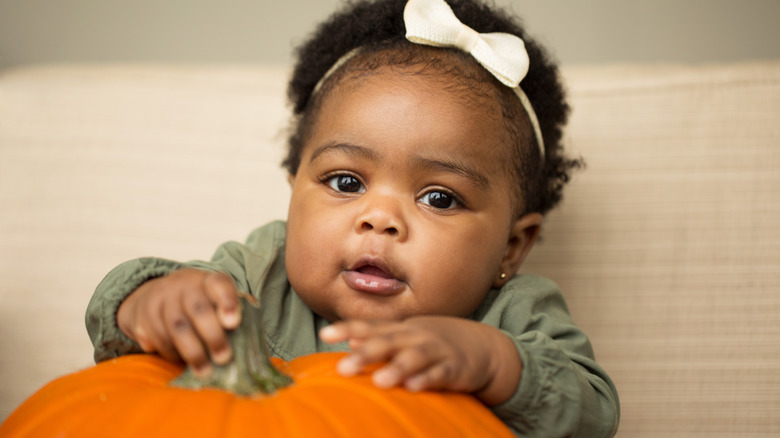 Baby girl touching pumpkin