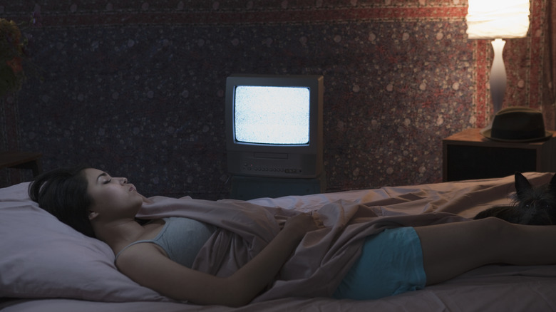 A woman sleeping in bed with TV on