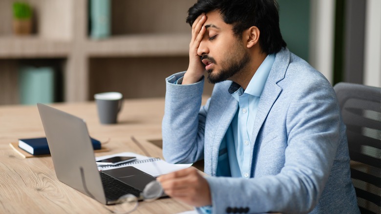 A tired man touching his face while working on his laptop