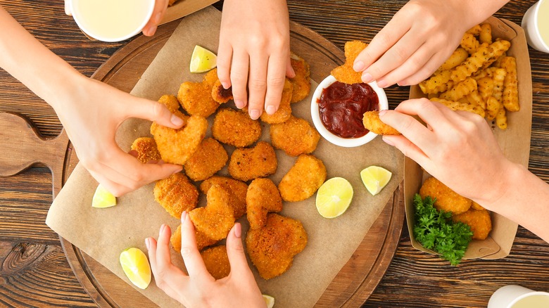 hands reaching for a plate of chicken nuggets