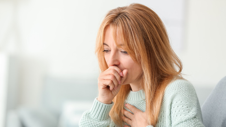 Woman coughing with hand on chest