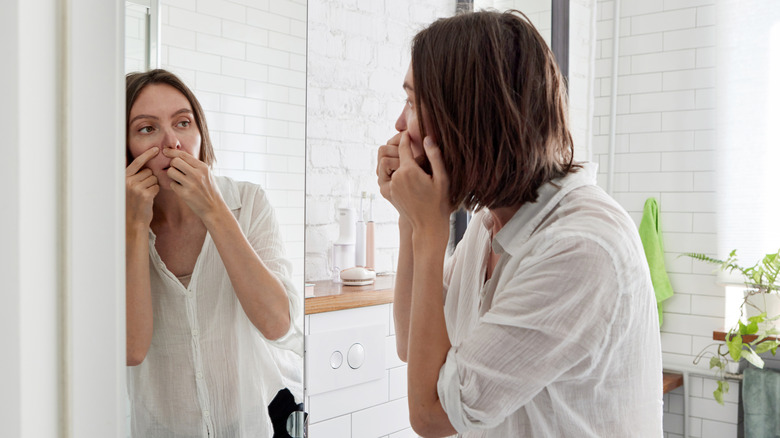 A woman looking in the mirror at something on her face