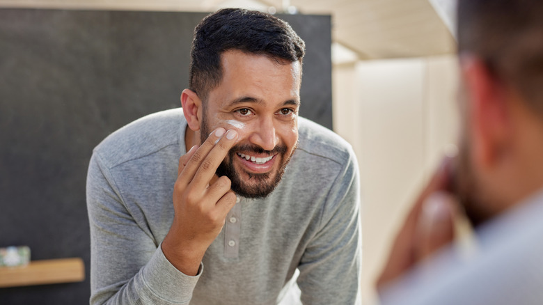 A man applying face cream while looking in the mirror