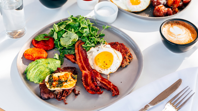 A plate with avocado, greens, bacon, eggs, and cheese