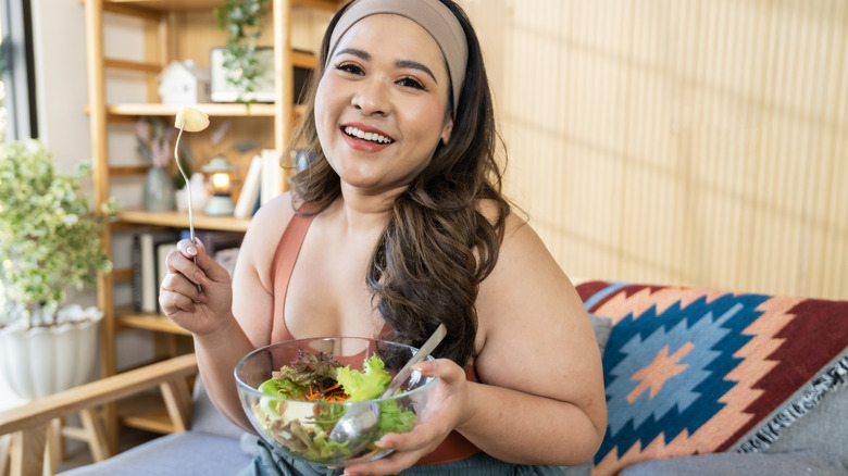 A woman eating a salad while sitting on a couch