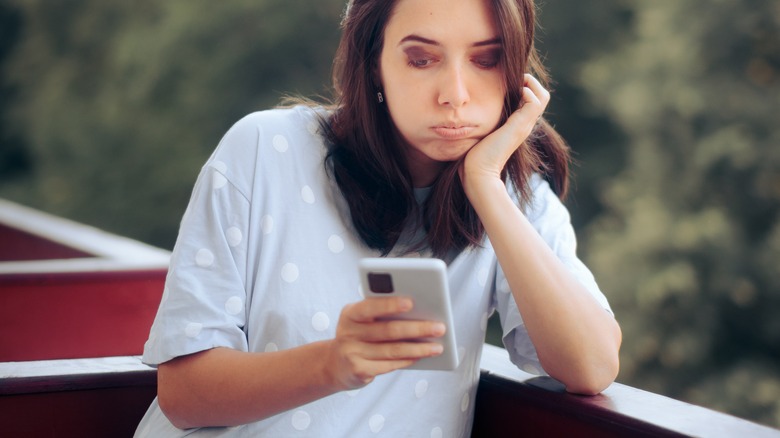 upset woman outside looking at phone 