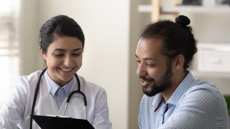 young male smiling with female doctor holding clipboard