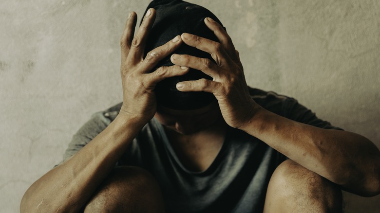 man holding head looking at the ground while sitting