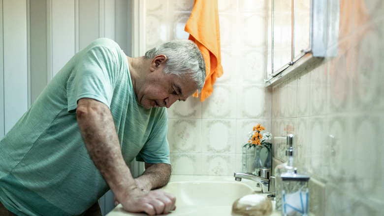 older man feeling sick in bathroom at sink