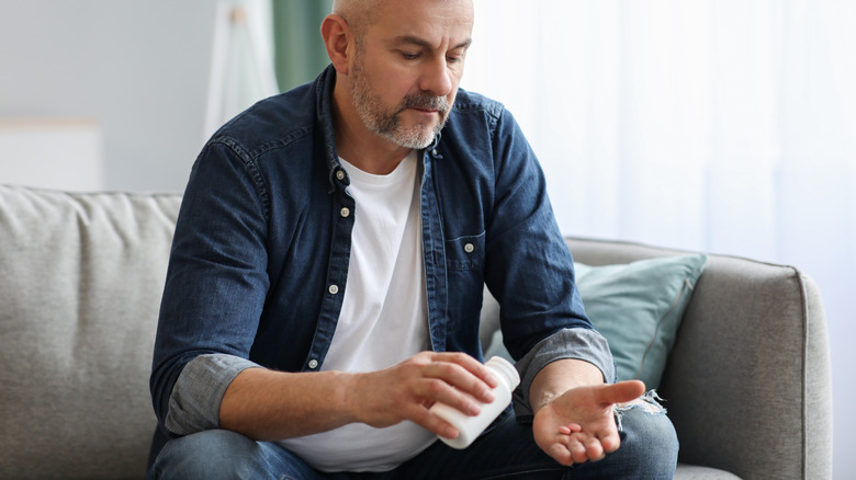 man sitting on couch looking at pills in his hand