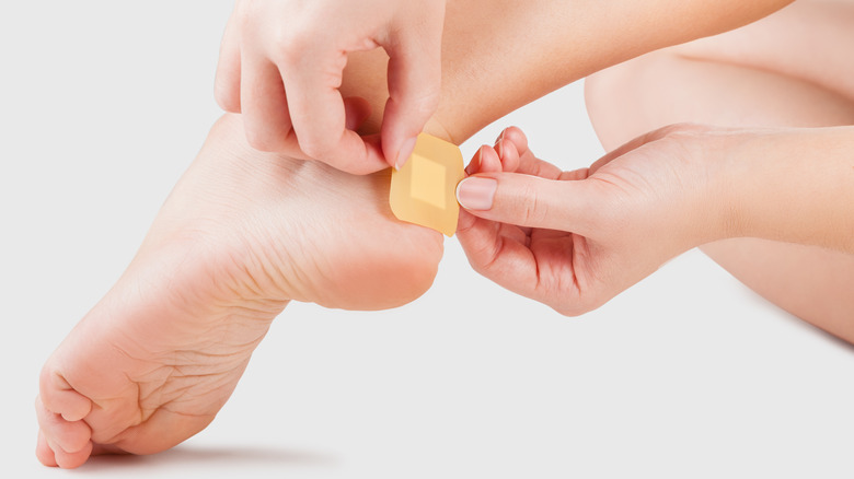 Woman putting band aid on blister on heel 