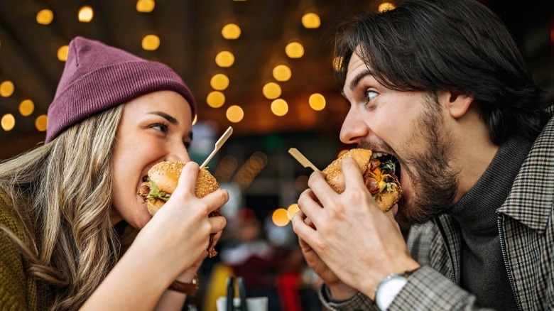 man and woman happily eating hamburgers