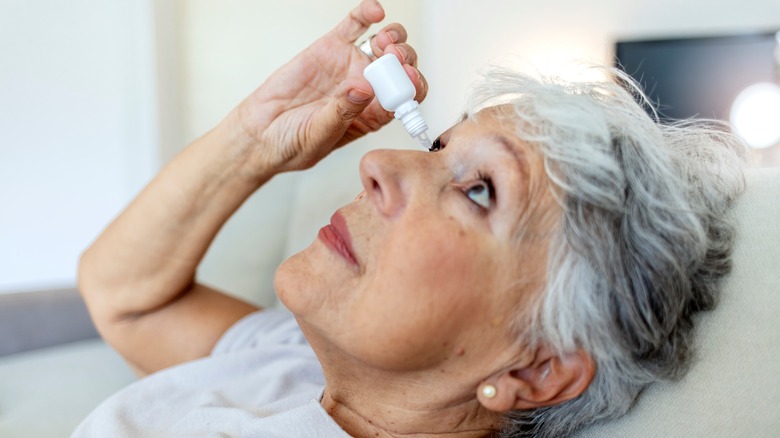 older woman after cataracts surgery putting eye drops in her eyes