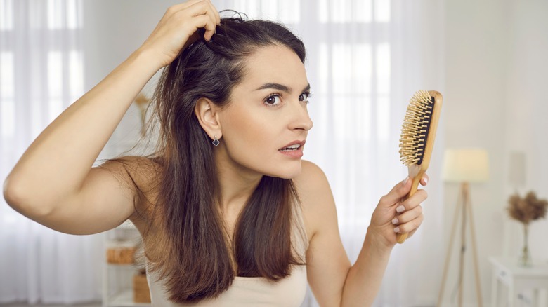 a woman experiencing hair loss looks in mirror 