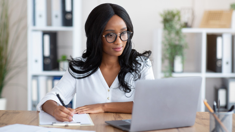 woman looking at laptop and taking notes