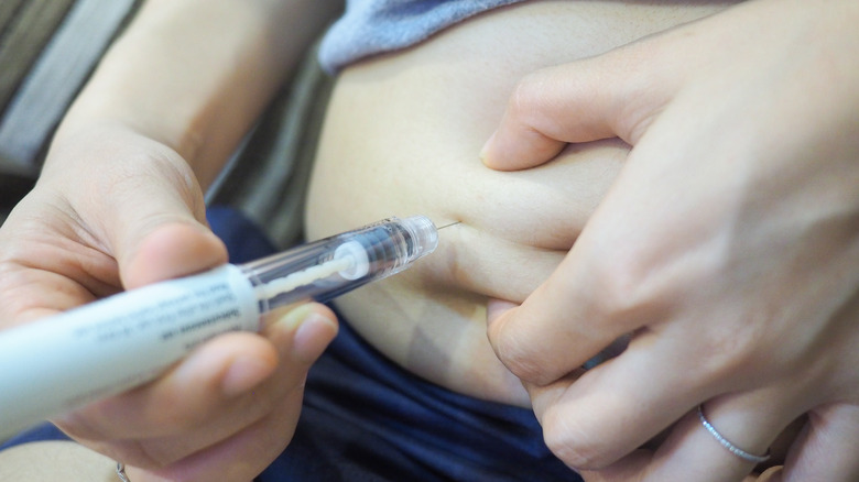 woman inserting needle in belly