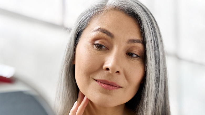 Woman with gray hair admiring her skin in the mirror