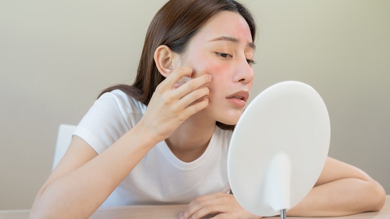 woman looking at skin in the mirror